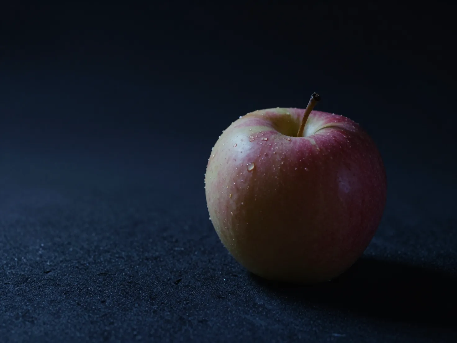 A single apple lit on a dark studio background